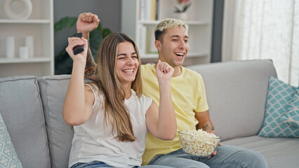 Canvas Print - Beautiful couple watching tv eating popcorn celebrating at home