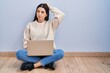 Young woman using laptop sitting on the floor at home confuse and wondering about question. uncertain with doubt, thinking with hand on head. pensive concept.