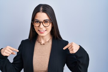 Poster - Young brunette woman standing over blue background looking confident with smile on face, pointing oneself with fingers proud and happy.