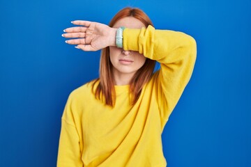 Poster - Young woman standing over blue background covering eyes with arm, looking serious and sad. sightless, hiding and rejection concept