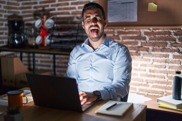 Wall Mural - Hispanic man with beard working at the office at night sticking tongue out happy with funny expression. emotion concept.