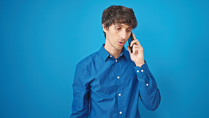 Poster - Young hispanic man talking on smartphone with serious expression over isolated blue background