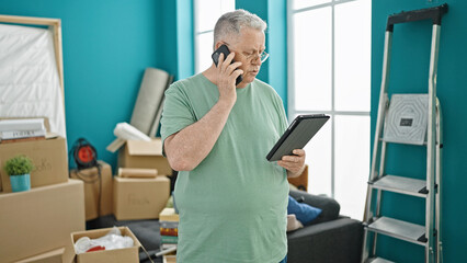 Wall Mural - Middle age grey-haired man talking on smartphone using touchpad at new home