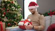 © Krakenimages.com - Young arab man unpacking gift sitting on sofa by christmas tree at home