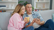 © Krakenimages.com - Man and woman couple drinking coffee using smartphone sitting on sofa at home