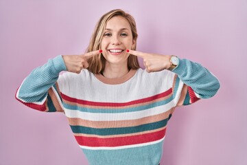 Poster - Young blonde woman standing over pink background smiling cheerful showing and pointing with fingers teeth and mouth. dental health concept.