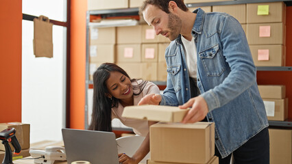 Two workers man and woman using laptop putting packages on table at office