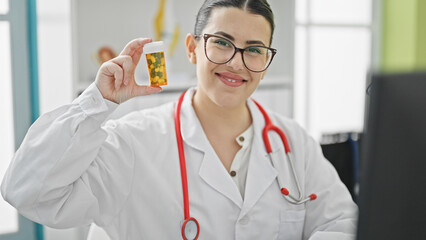 Sticker - Young beautiful hispanic woman doctor holding bottle of pills at the clinic