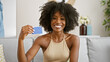 African american woman holding credit card sitting on sofa at home