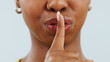 Black woman, mouth and lips in secret for gossip, privacy or confidential information against a studio background. Closeup of African female person with finger or emoji in silence, quiet or whisper