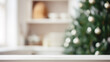 Leerer weißer Holztisch in Küche, weihnachtlich geschmückter Tannenbaum mit Lichterkette im verschwommenen Hintergrund, Platz für Warenpräsentation oder Text