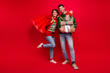 Poster - Full body portrait of two positive people hold boutique bags pile stack newyear giftbox isolated on red color background