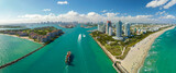 Fototapeta  - Commercial container ship entering Miami port harbor through main channel near South Beach. Luxurious hotels and residential buildings on waterfront and high skyscraper towers of downtown in distance