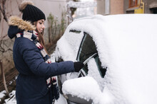Side view of pretty female cleaning car from snow. Woman preparing for driving in the morning