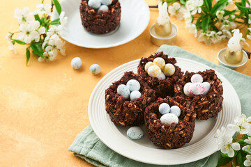 Wall Mural - Easter chocolate nest cake with mini chocolate candy eggs with blossoming cherry or apple flowers on yellow background table. Creative recipe for Easter table with holiday decorations. Top view.