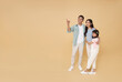 Happy asian father and mother hugging daughter and hand pointing finger isolated on nude color copy space background. family fun portrait