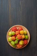 Wall Mural - surinam cherries, eugenia uniflora, aka pitanga, brazilian or cayenne cherry, vibrant colorful fruits on wooden plate, isolated on black rustic background surface with copy space