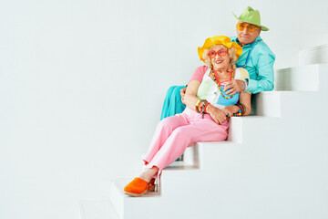 Wall Mural - Beautiful senior old couple wearing fancy party clothes acting in studio on a colored background. Conceptual image about third age and seniority, old people feeling young inside.