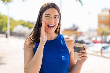 Wall Mural - Young pretty Brazilian woman holding a take away coffee at outdoors shouting with mouth wide open