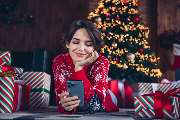 Wall Mural - Photo of pretty young girl lying floor read post hold gadget wear trendy red sweater festive interior living room presents christmas tree