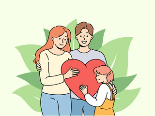 Strong family of loving parents and little pre-teen girl hold big heart. Happy spouses hug celebrating family day and rejoicing that they have become mother and father for child from orphanage.