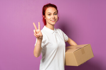 Wall Mural - Teenager delivery girl isolated on purple background smiling and showing victory sign