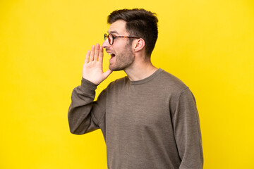 Wall Mural - Young caucasian man isolated on yellow background shouting with mouth wide open to the side