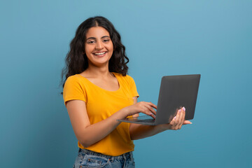 Portrait of confident young indian woman holding and using laptop