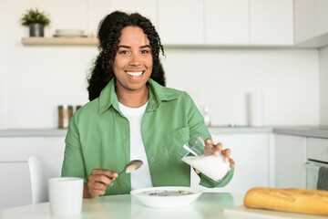 Wall Mural - african woman pouring milk into bowl with cereals in kitchen