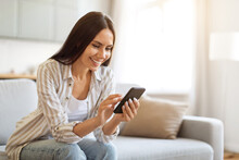 Smiling Young Woman Using Smartphone While Resting On Couch At Home