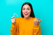 Young caucasian woman holding invisible braces isolated on blue background with shocked facial expression