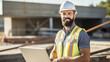 © BlazingDesigns - Portrait of young caucasian hardworking smiling bearded supervisor with helmet on head in vest and with laptop in hands posing on construction site.