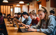 © piai - Teen students learning on laptop computers in ful modern classroom with wooden desks