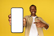 Cheerful young black guy in casual pointing finger at mobile smartphone with empty screen
