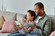 © LIGHTFIELD STUDIOS - happy african american father and son in casual outfits sitting on sofa looking at mobile phone