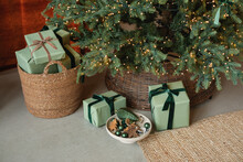 Stack Of Wrapped Christmas Gifts In A Basket And Under An Illuminated Christmas Tree In A Living Room