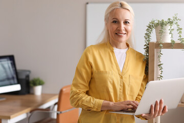 Wall Mural - Mature female programmer working with laptop in office