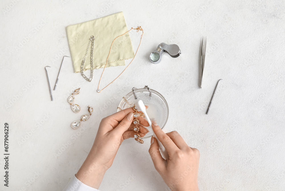 Woman cleaning beautiful bracelet with toothbrush on light background