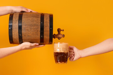 Woman pouring beer from barrel into mug on yellow background