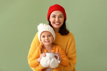 Wall Mural - Young mother and her little daughter with mug of hot chocolate on green background