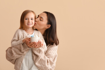 Wall Mural - Young mother and her little daughter with mug of hot chocolate on beige background