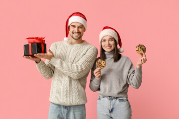 Canvas Print - Young couple in Santa hats with gift boxes and tasty cookies on pink background