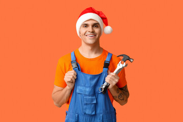 Wall Mural - Male plumber in Santa hat with hammer and wrenches on orange background