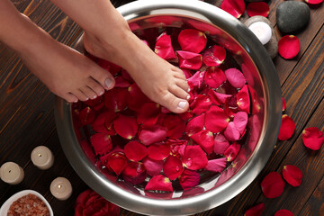 Wall Mural - Woman soaking her feet in bowl with water and red rose petals on wooden floor, top view. Pedicure procedure