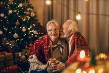 A Festive Senior Couple Is Sitting On The Floor At Christmas And New Year's Eve, Kissing, Hugging And Giving Gifts.
