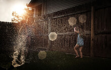Sisters Playing In Sprinkler In Yard