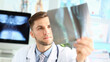 Portrait of thoughtful doc examining x-ray picture. Concentrated physician making diagnosis. Medical treatment and health care concept. Blurred background