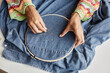 © Seventyfour - Above angle of hands of young creative woman making embroidery with beads on back of denim jacket while sitting by workplace