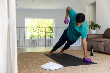 Biracial man exercising with dumbbells on mat at home, copy space