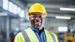© BlazingDesigns - Portrait of a happy African American factory worker wearing hard hat and work clothes standing besides the production line.